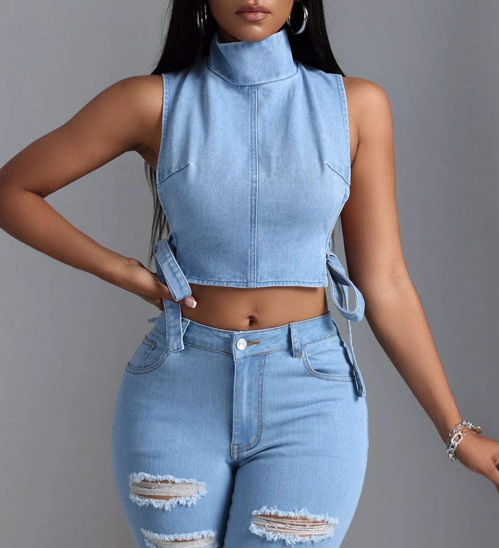 Person wearing a light blue denim sleeveless top and high-waisted jeans with a gray background