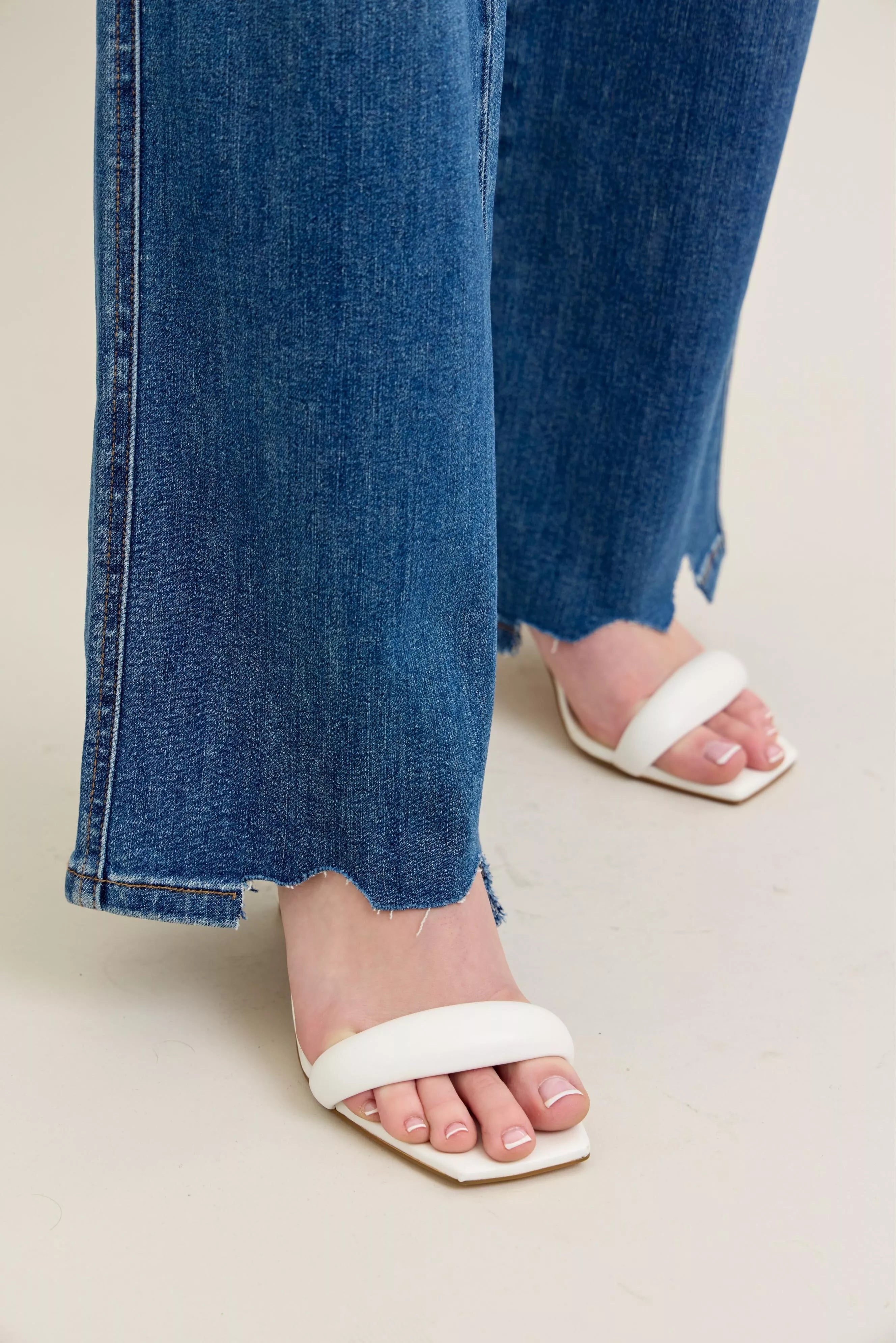 White sandals worn with blue jeans on a neutral background