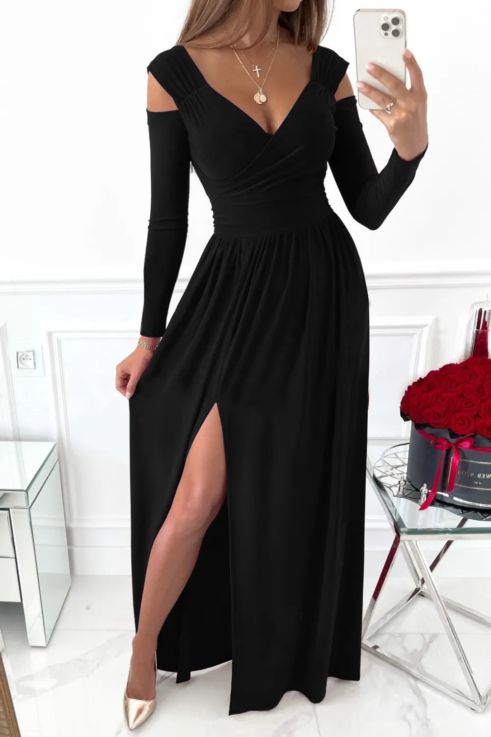 Woman wearing a black dress with long sleeves and a slit, taking a selfie.
