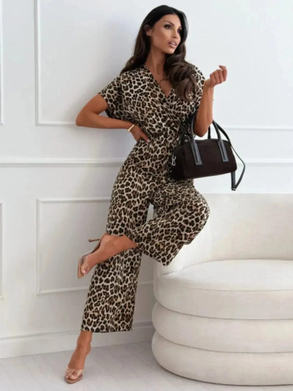 Woman in leopard print outfit holding a brown handbag against a white wall.