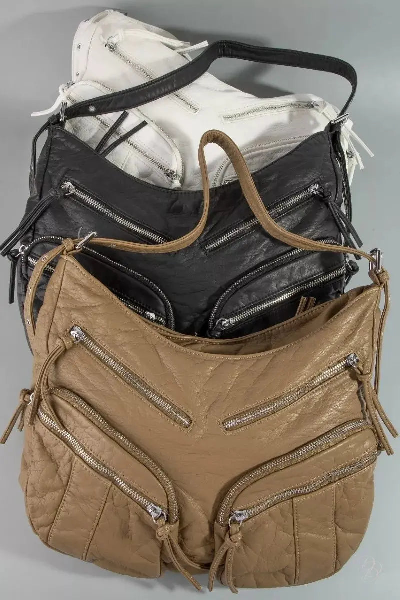 Stack of bags including a brown leather handbag, black leather bag, and white bag on a gray background