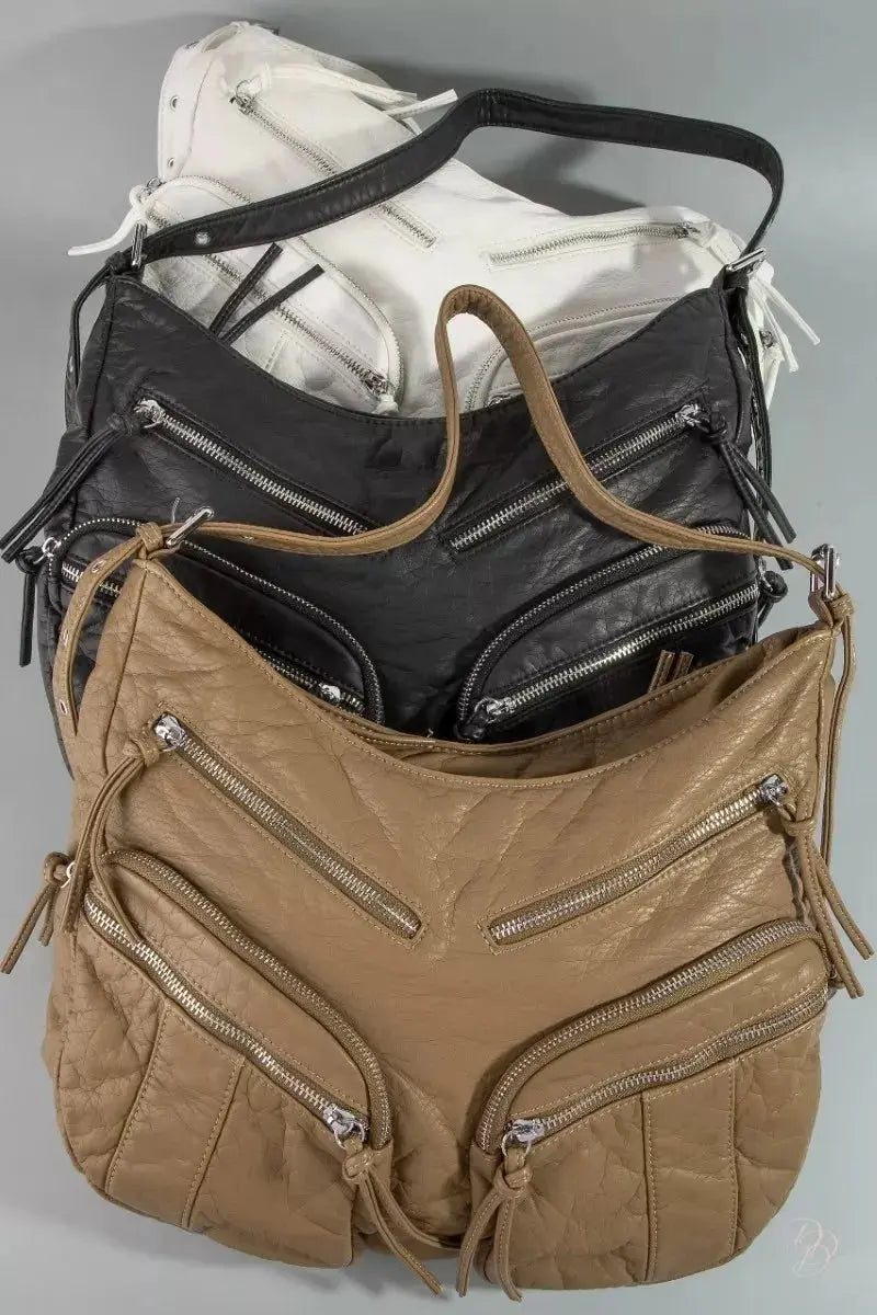 Stack of bags including a brown leather handbag, black leather bag, and white bag on a gray background