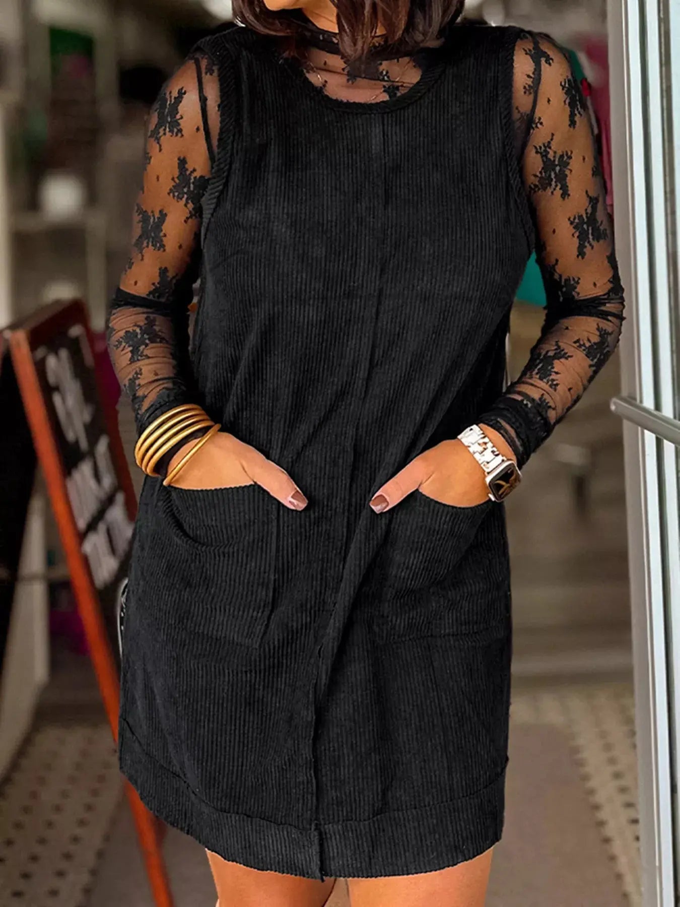 Person wearing a black sleeveless dress with floral patterns on sleeves and hands.