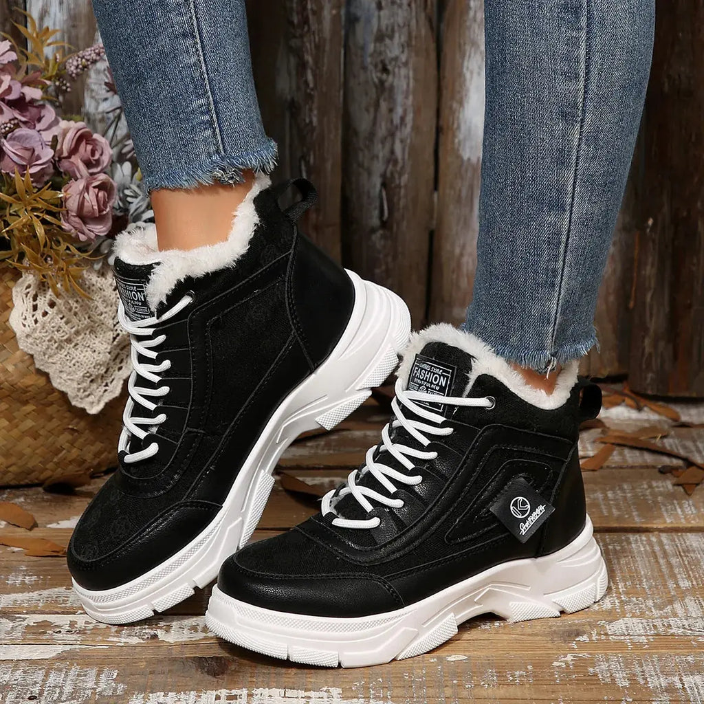 Black winter boots with white soles worn by a person on a wooden surface