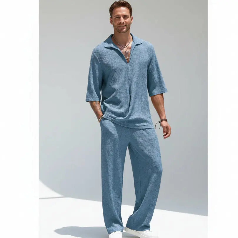 Man wearing a blue textured outfit standing outdoors on a tiled patio.