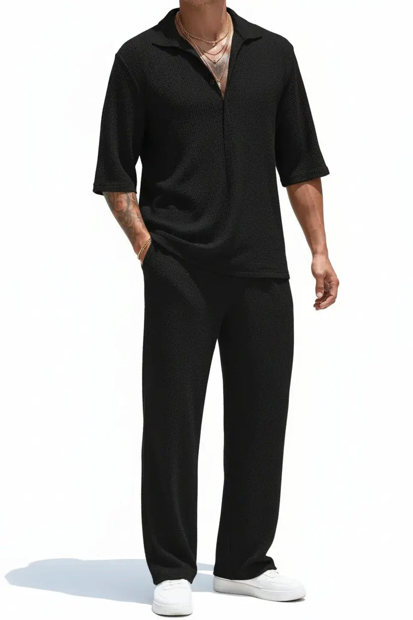 Person wearing a black outfit standing on a tiled patio with greenery in the background