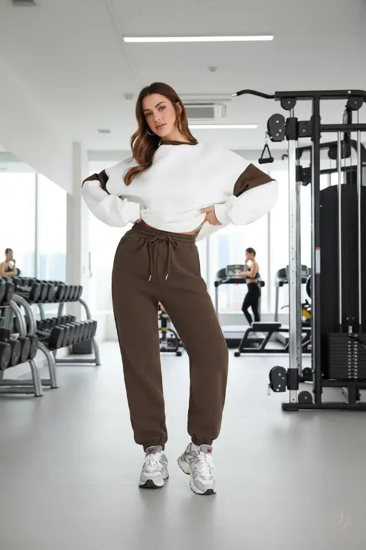 Woman in a white top and brown pants standing in a gym.