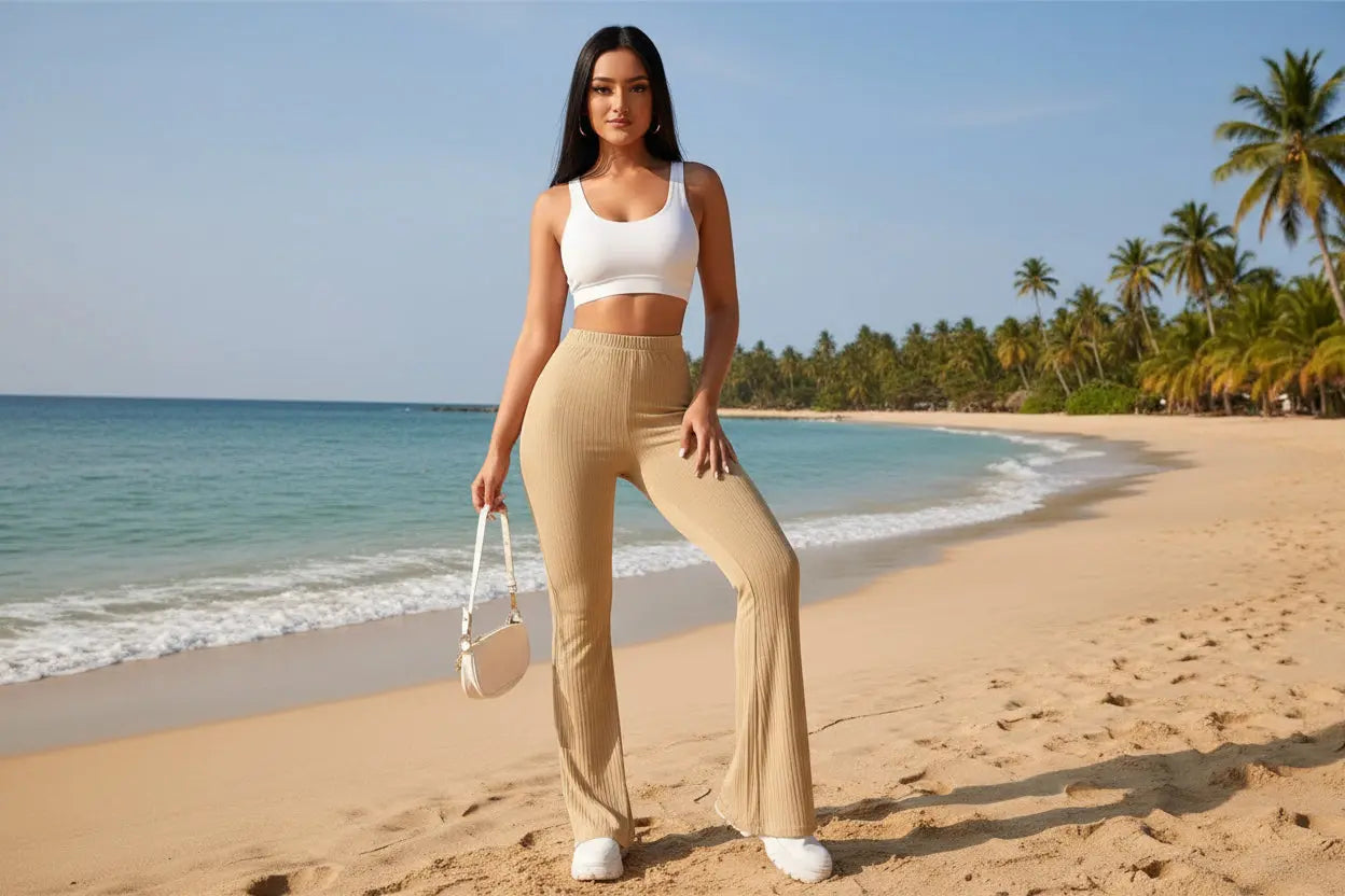 Woman wearing a floral blouse and beige pants standing against a neutral background with plants.