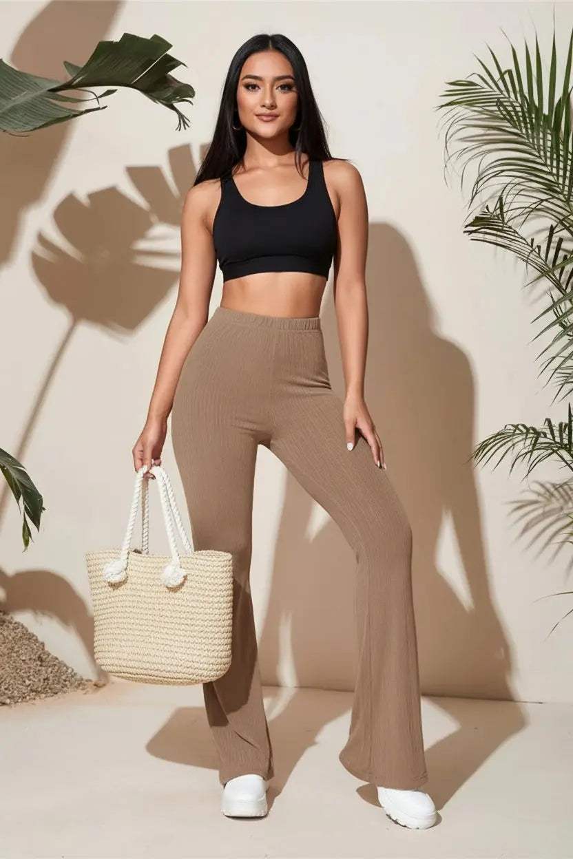 Woman wearing a floral blouse and brown pants standing against a neutral background with plant